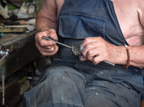 Close up on man's hands with threading die. Blurred background, soft selective focus. The man is decked out in dirty working clothes sitting at the home workbench. Image of man at work process
