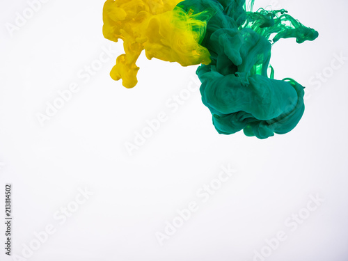 Movement of yellow and green acrylic droplets in liquid. Two droplets of colourful ink in water, an abstract banner. Yellow-green acrylic swirl in liquid, isolated on white background