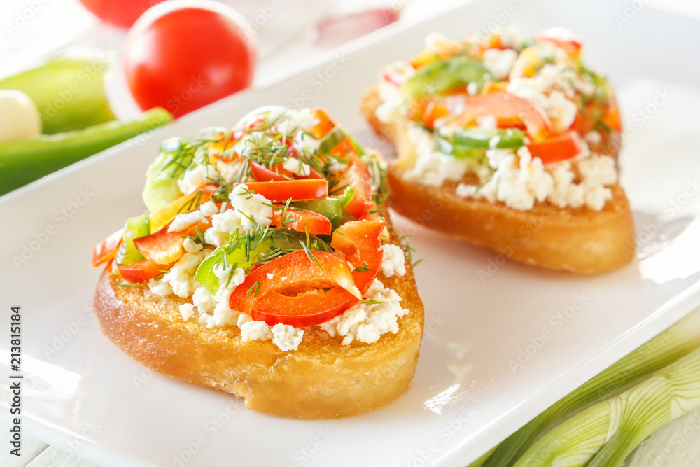 Two Bruschetta with red sweet pepper and goat cheese in a plate next to fresh vegetables on white boards. Close-up Two Bruschetta with red sweet pepper and goat cheese in a plate next to fresh vegetables on white boards. Close-up
