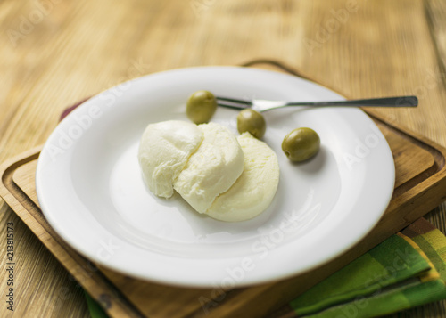 Cheese mozzarella and olives on a plate on a wooden background.