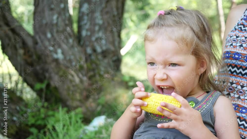 Little kid girl on family nature picnic eating bite a yellow boiled cooked corn Little kid girl on family nature picnic eating bite a yellow boiled cooked corn