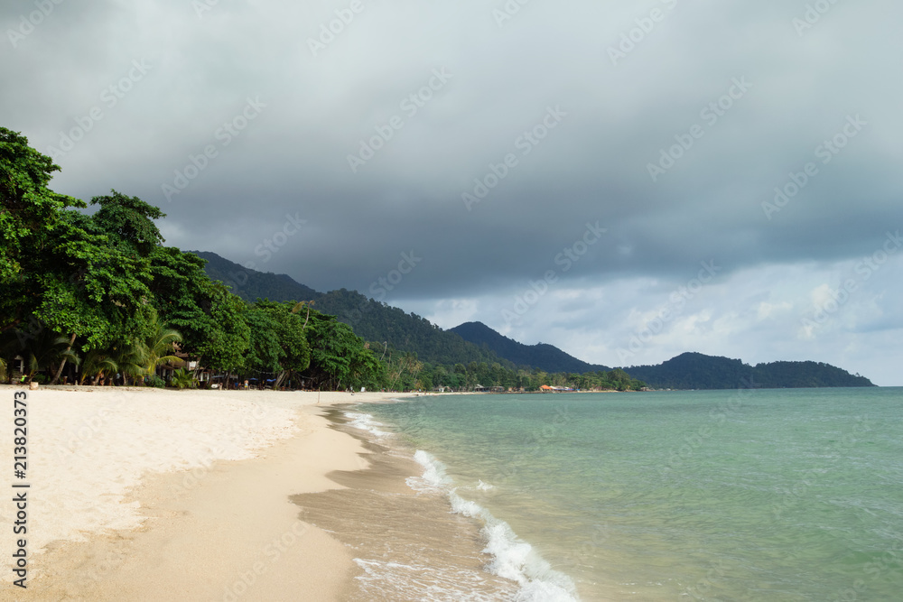 Tropical landscape with blue sea, sandy beach, palm trees and cloudy sky in a stormy weather. Koh Chang, Thailand.