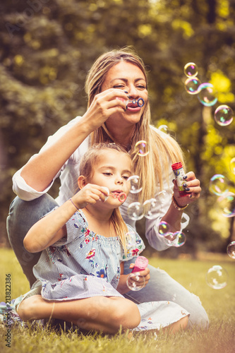 Happy mother and daughter at nature have fun blowing bubbles.