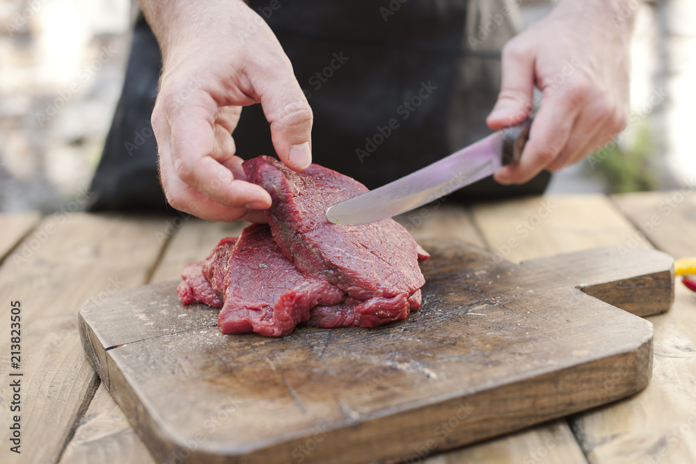 Men's hands and steaks of meat. Preparation of dinner man. Wooden table and old board. Copy space.