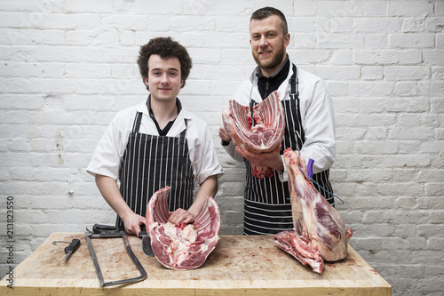 Two butchers side by side holding meat joints, part of a large butchered carcass.