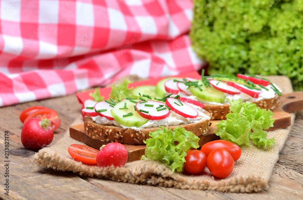 Grain bread with spread, fresh radish, cucumber and tomatoes on - concept of healthy fitness breakfast or snack, fresh salad in the background