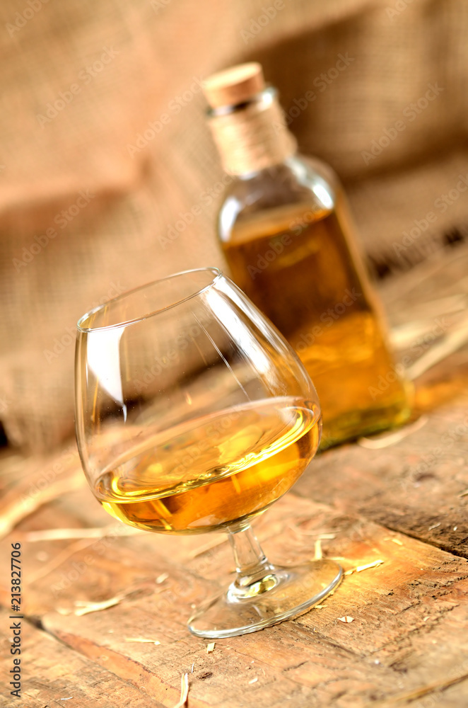 Glass of cognac on rustical wooden background and bottle in background vertical photo Glass of cognac on rustical wooden background and bottle in background vertical photo