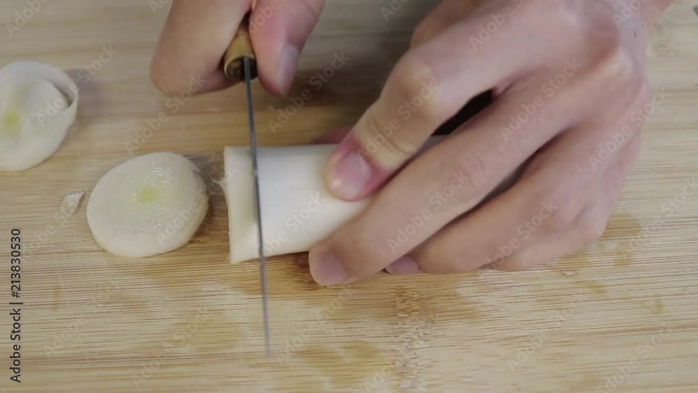 Someone cooking in the kitchen counter. He is cutting a vegetable, a leek, with a knife. Someone cooking in the kitchen counter. He is cutting a vegetable, a leek, with a knife.