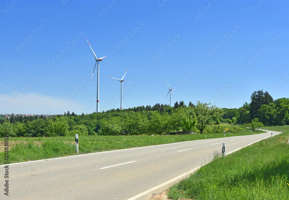 Lush green landscape with grass, trees, road and three new windmills under blue sky near Stuttgart, Germany