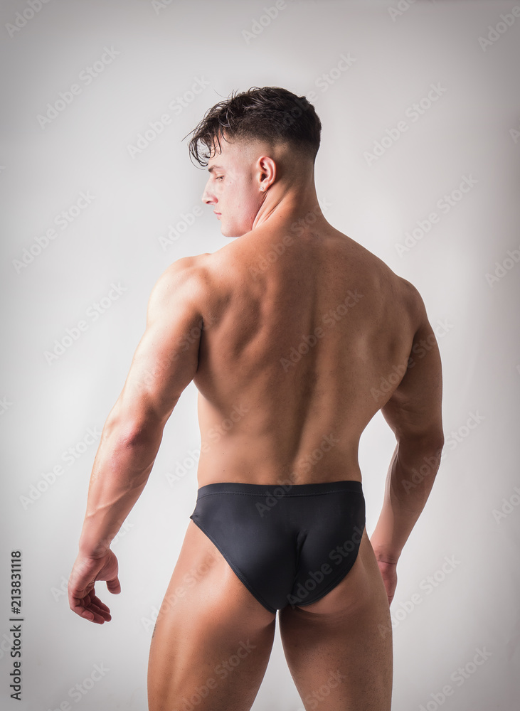 Rearview of Young Gym Fit Man Showing His Sexy Back While Looking To a Side. on Light Background in Studio