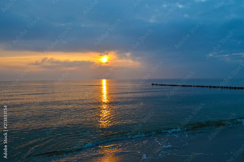 Fototapeta premium Blue and orange light while a sunrise over the Baltic Sea on Usedom, Germany, with wave-breakers and seagulls sitting on them against the light