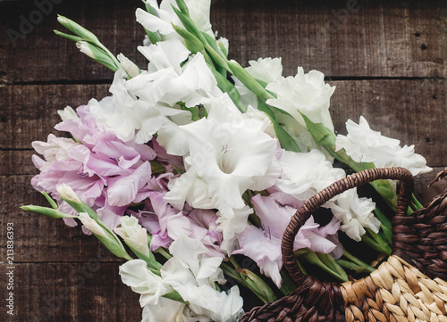 beautiful pink and white gladioluses in stylish wicker basket on rustic wooden background flat lay. colorful gladioli on rustic wood, space for text, greeting card. spring image. instagram photo