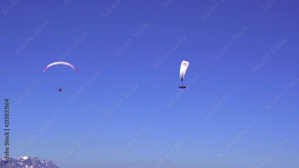 Two paragliders in slow motion flying over a mountain range.