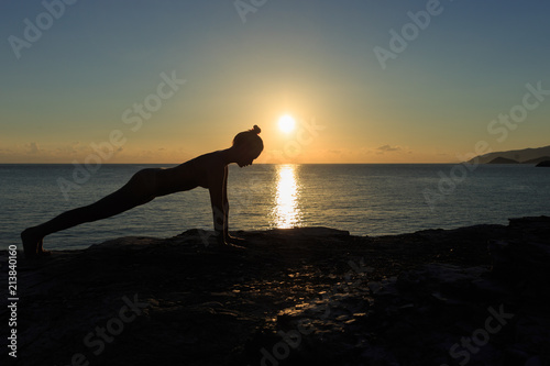 Young female silhouette doing plank exercise on a beach at sunrise. photo