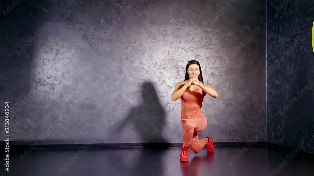 female fitness trainer is squatting with lunges in a gymnastic room and smiling, looking in a camera female fitness trainer is squatting with lunges in a gymnastic room and smiling, looking in a camera