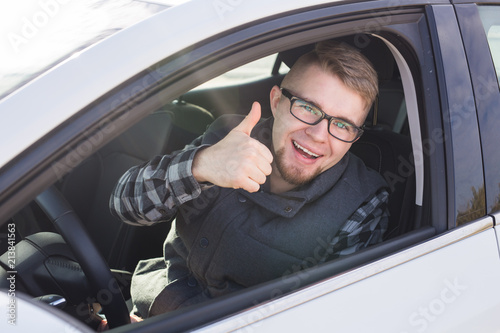 Cheerful casual guy smiling happily showing thumbs up sitting in a big white car © satura_