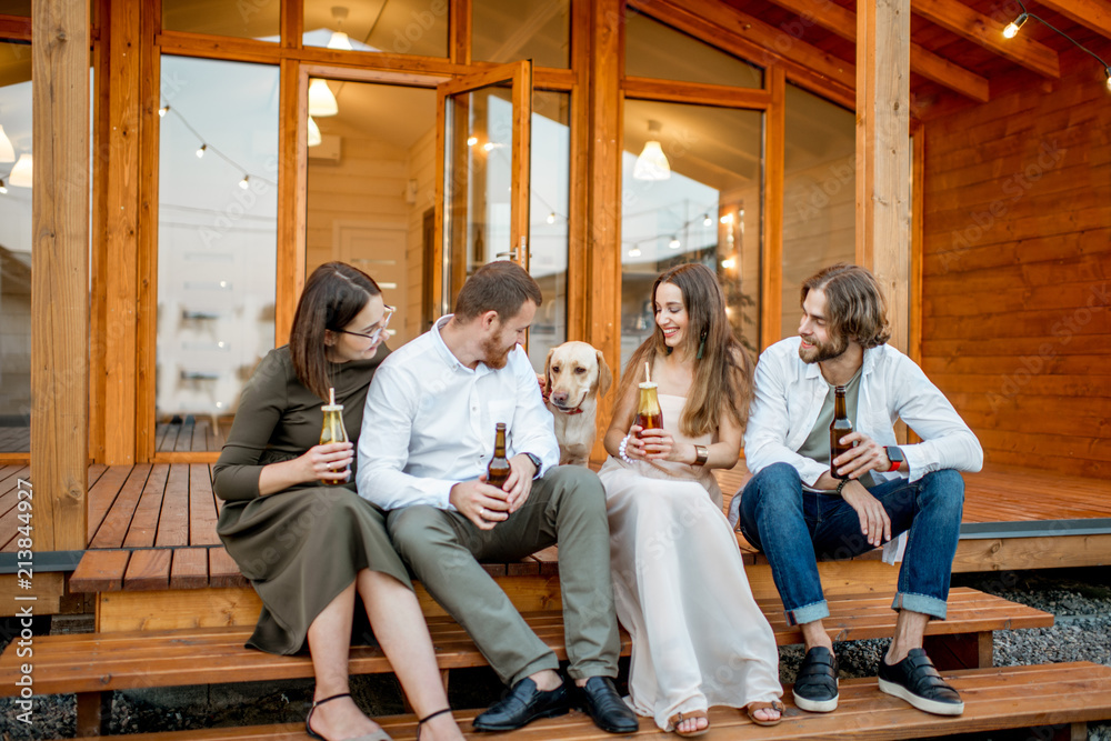 Young friends enjoying evening time sitting together with dog on the terrace of the modern wooden house