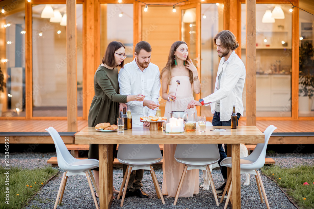Four friends enjoying evening time having a dinner on the backyard of the modern country house outdoors Four friends enjoying evening time having a dinner on the backyard of the modern country house outdoors