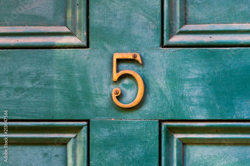 House door number 5 in bronze on an older wooden painted green door