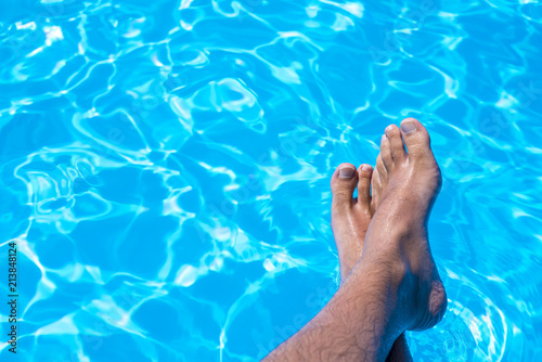 Top view of man feet in the swimming pool as concept for summertime