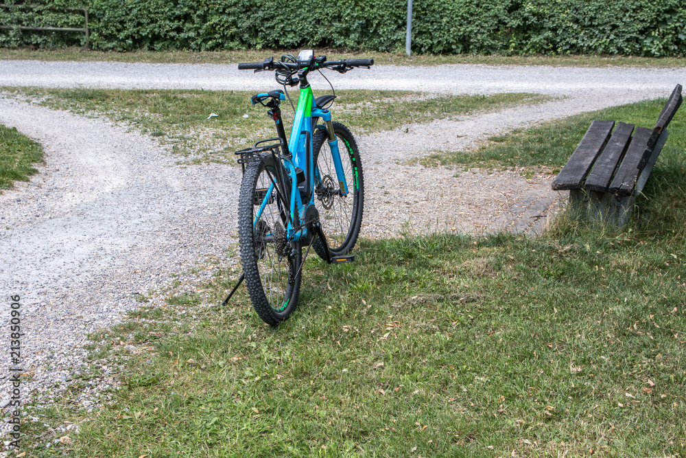 Fototapeta premium Fahrrad steht auf Kiesweg, Weggabelung mit Bank