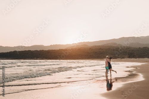 Young man and woman kissing on beach at sunset. Horizontal warm color portrait