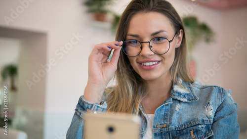 Pretty smiling young woman in glasses using modern smartphone, chatting with friends online, lifestyle concept photo