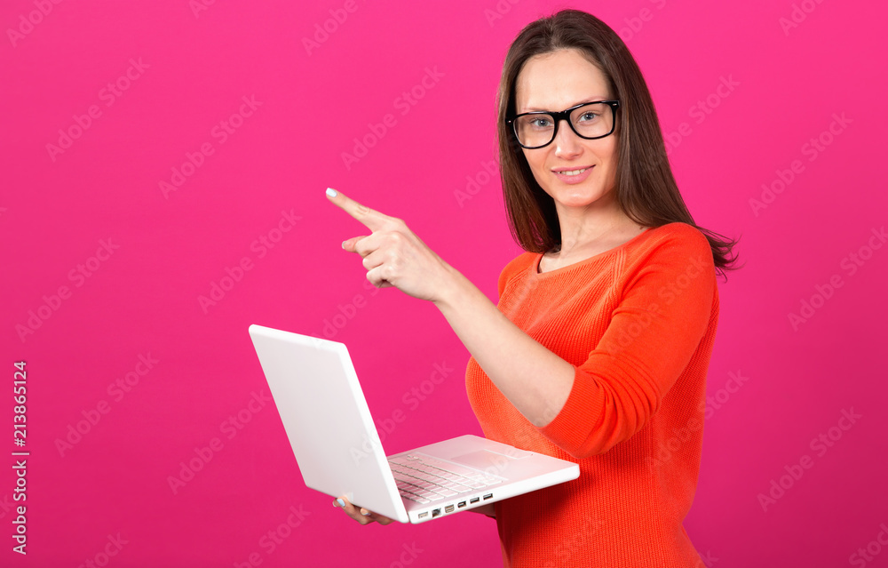 Beautiful brunette woman with glasses. Young woman 25 years old with a laptop in her hands showing a finger up standing on a pink background. Online shopping. Beautiful brunette woman with glasses. Young woman 25 years old with a laptop in her hands showing a finger up standing on a pink background. Online shopping.
