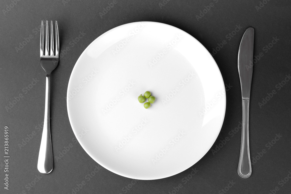 a few green fresh peas on a white plate next to a fork and knife on a black background. The concept of diet. a few green fresh peas on a white plate next to a fork and knife on a black background. The concept of diet.