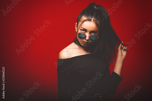 Obraz na plátně Portrait of cool crazy brunette fashionable girl in sunglasses, casual hairdo on red background