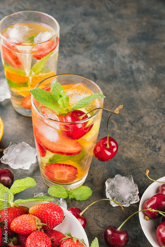 The glasses of lemon water. Lemonade with strawberry, mint and ice on a table. Sunny summer day. Copy spase