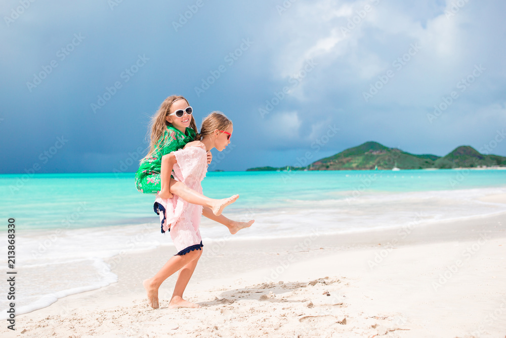 Little happy funny girls have a lot of fun at tropical beach playing together. Sunny day with rain in the sea