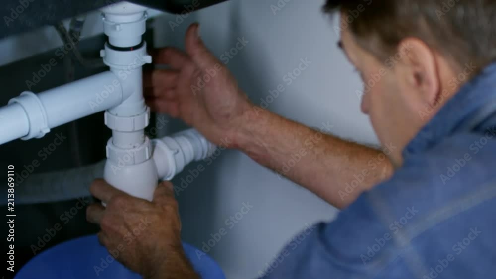 Tilt up of male plumber unscrewing drain pipe under sink and cleaning