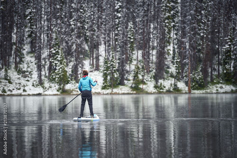 a woman paddle boarding on a mountain lake in the winter a woman paddle boarding on a mountain lake in the winter