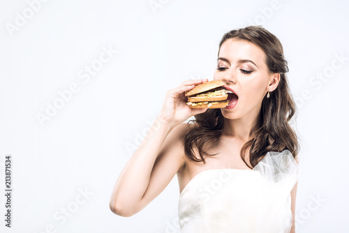 hungry young bride in wedding dress eating big burger isolated on white