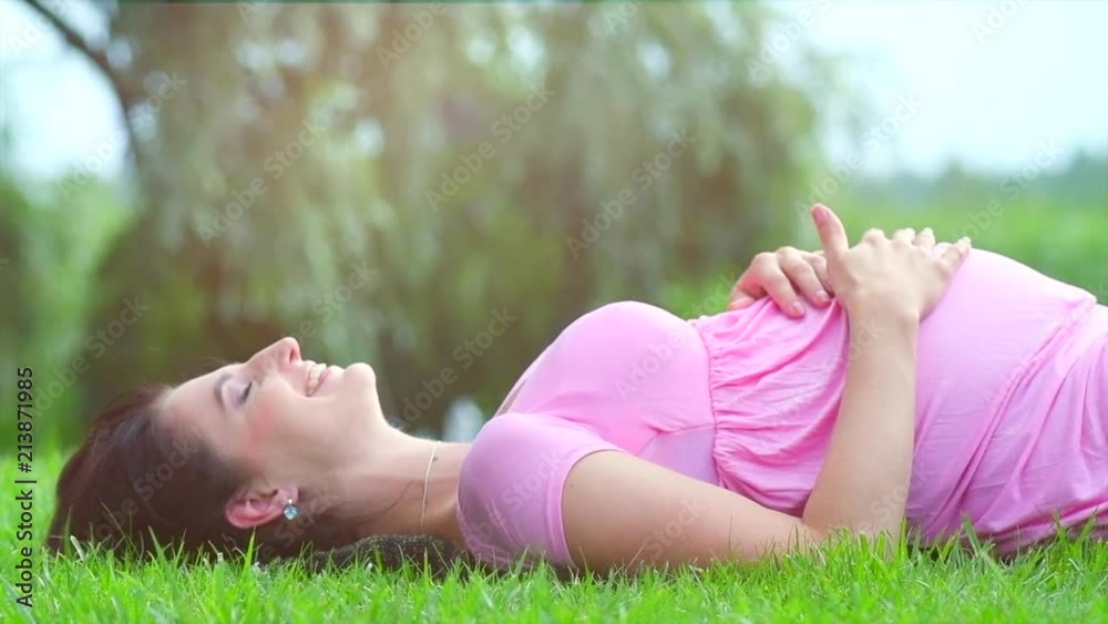 Happy pregnant woman touching her belly. Pregnant mother lying on green grass, enjoying nature, caressing her belly, smiling. Healthy pregnancy concept. Slow motion 4K UHD video 3840x2160 Happy pregnant woman touching her belly. Pregnant mother lying on green grass, enjoying nature, caressing her belly, smiling. Healthy pregnancy concept. Slow motion 4K UHD video 3840x2160