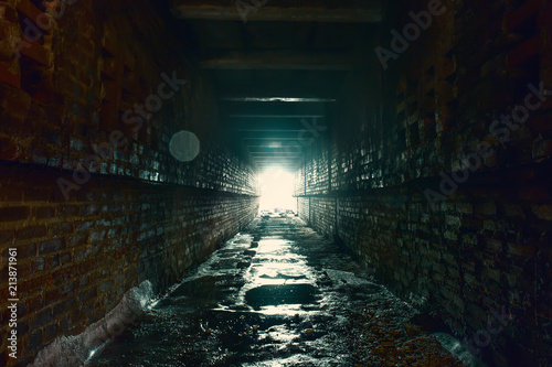 Light and exit in end of dark long brick abandoned industrial tunnel or corridor or sewer channel, way to freedom concept