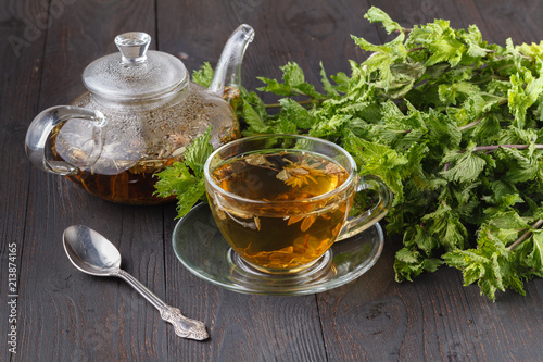 Glass teapot and cup with green tea on old wooden table with fresh herbs