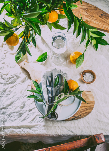 Table setting with white plate, cutlery, linen napkin and orange tree branch decoration on white linen tablecloth . Close up. Table with table setting and shair photo