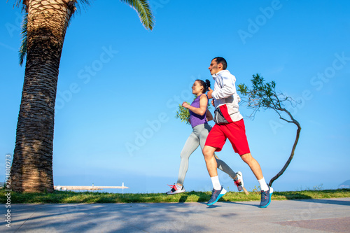 Running couple jogging on beach. Runners training together. Man and woman joggers exercising outdoors.