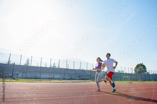 Young sportive couple warming up legs before jogging on running track at sports stadium © blicsejo