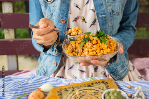 Woman holds and tastes Indian chickpea salad with grated carrot, onion, garlic paste, tahini sesame seeds paste and fresh green herbs. Vegan, vegetarian healthy food.