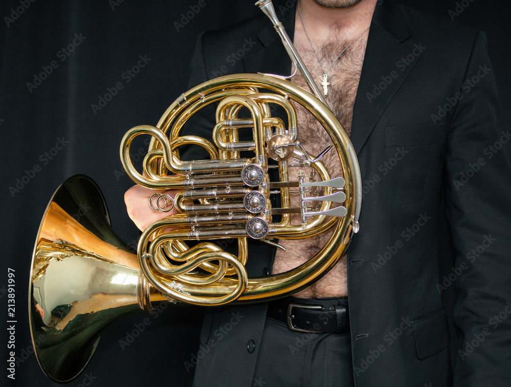 Fototapeta premium A man in a jacket on his naked body, holding a musical instrument. (Waldhorn)
