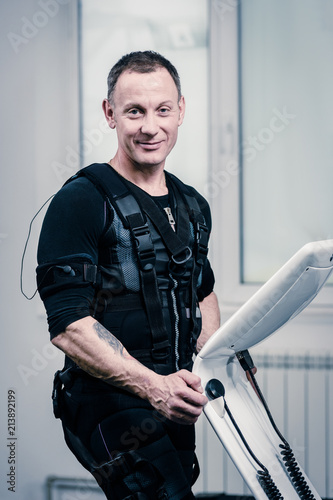 Portrait of athletic man in EMS suit near electro muscle stimulation machine photo