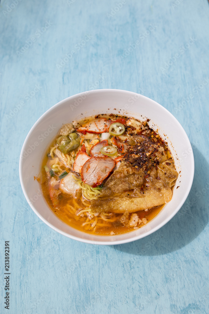 Thai style spicy Tom yum egg noodle with roasted pork soup on blue table background