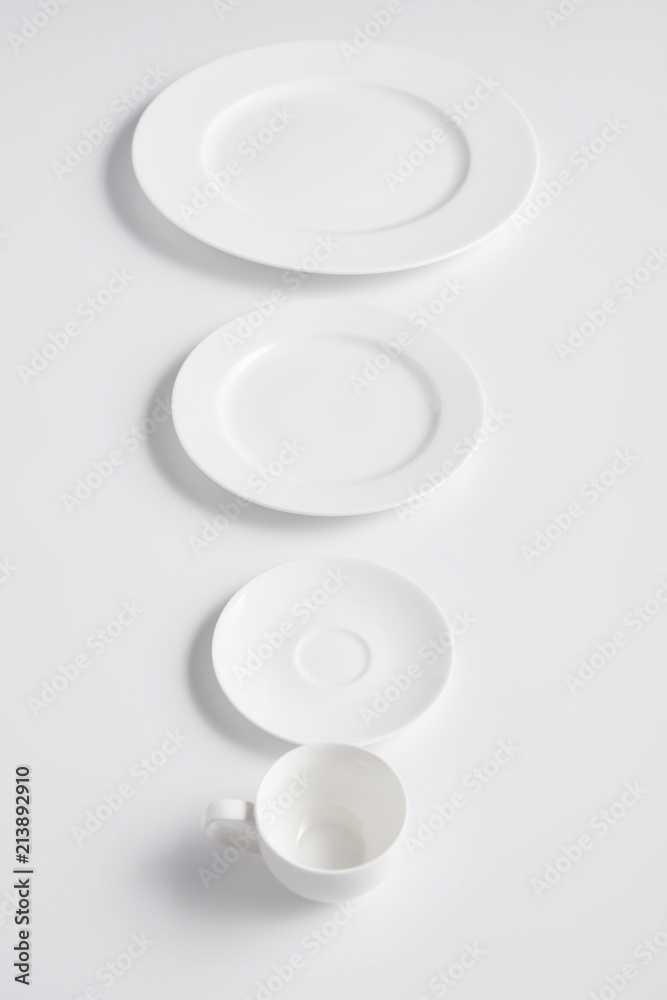 selective focus of arranged various plates and cup on white table selective focus of arranged various plates and cup on white table