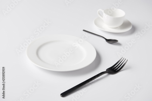 selective focus of plate, fork, spoon and cup on white table