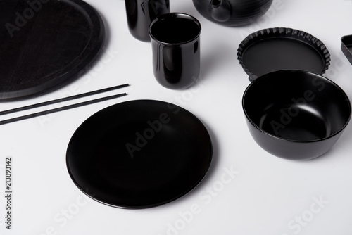 selective focus of black plate, bowl, cups, chopsticks, baking dish and tray on white table