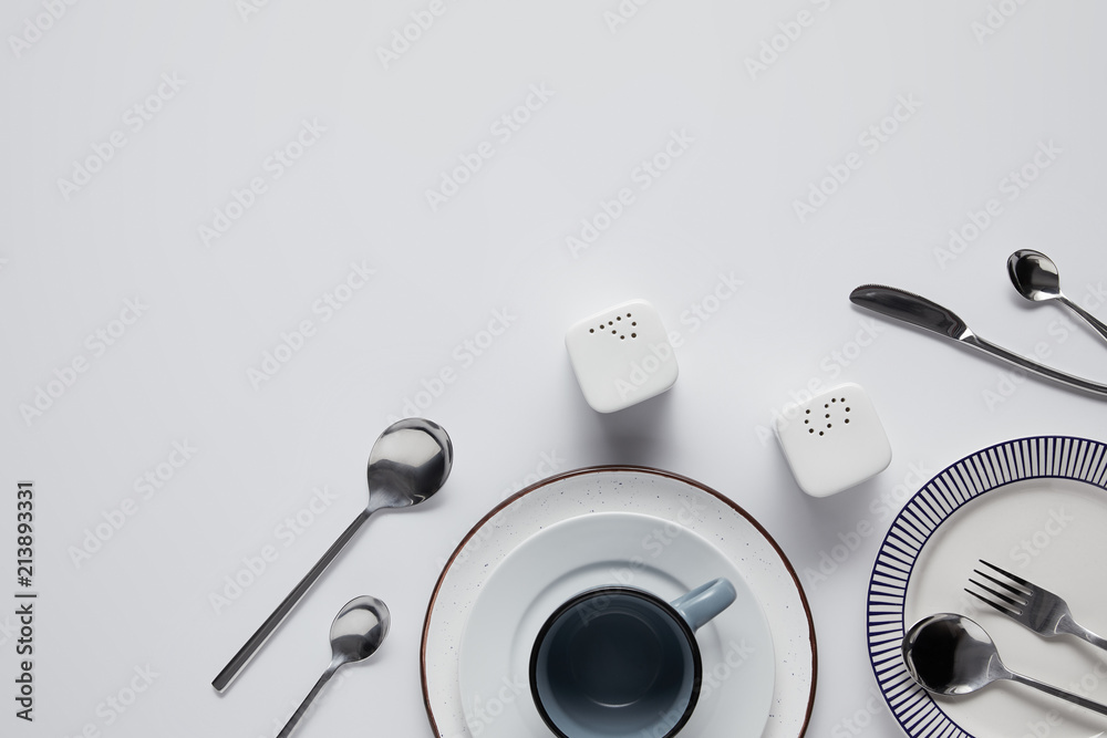 top view of saltcellar, pepper caster, spoons, knife, fork, cup and plates on white table top view of saltcellar, pepper caster, spoons, knife, fork, cup and plates on white table