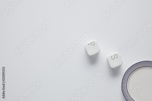 top view of plate, saltcellar and pepper caster on white table, minimalistic concept